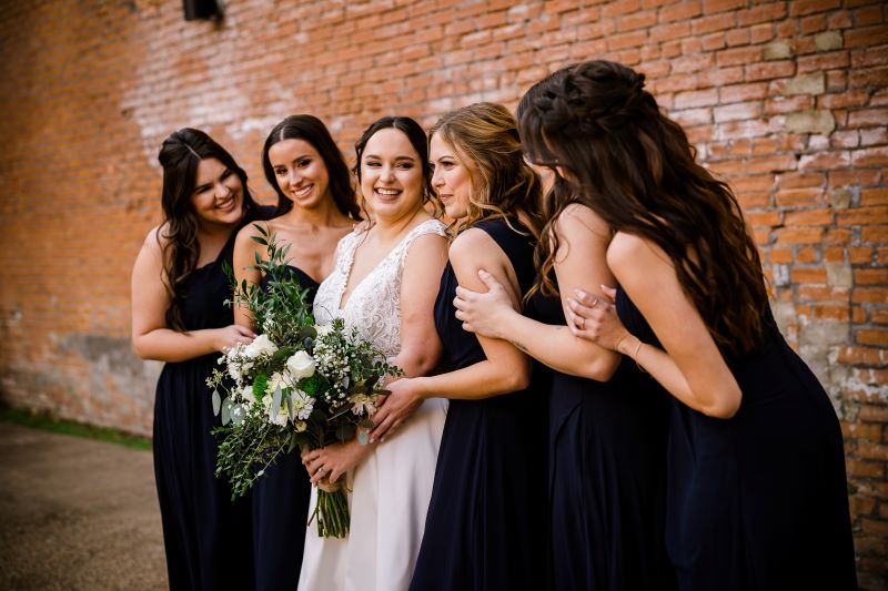 Bridesmaids posing for portrait in front of brick wall in outdoor area.