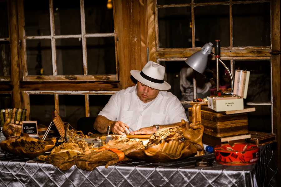 Man in hat cutting cigars at table in the Event Hall.