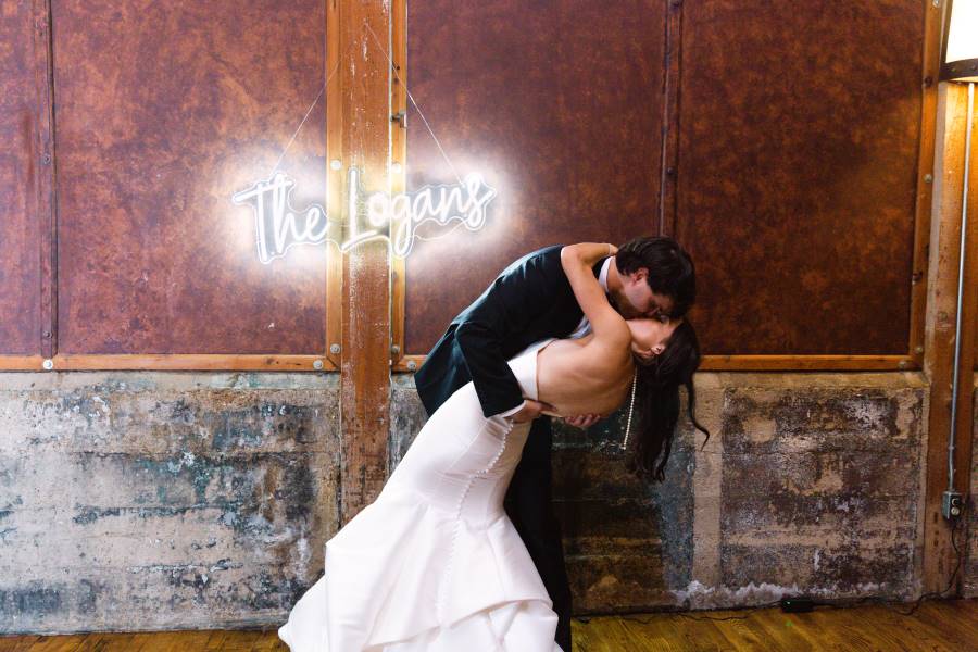 Bride and groom kissing in front of sign that says "The Logans."