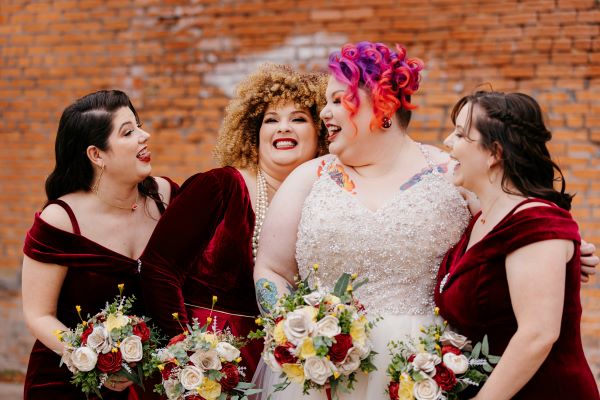 Bridesmaids laughing in front of brick wall in the outdoor Dye Room.