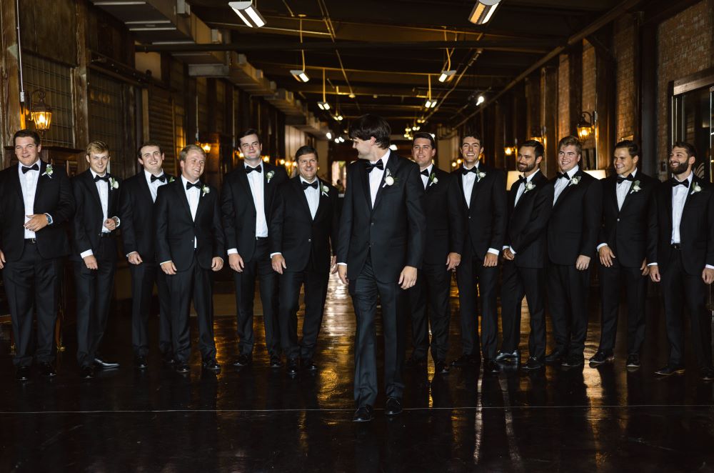 Groom and groomsmen in tuxedos pose for portrait in the Grand Hall.