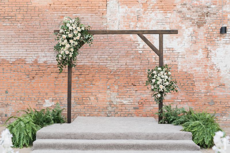 Handcrafted wooden altar with flowers on it in front of brick background.