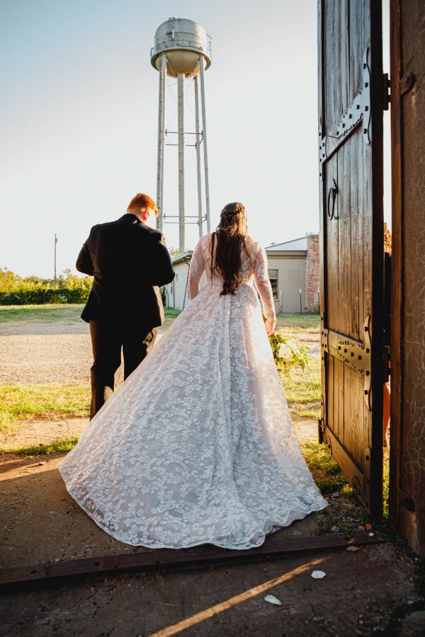 Wedding couple walking through large wooden doors with water tower in background.