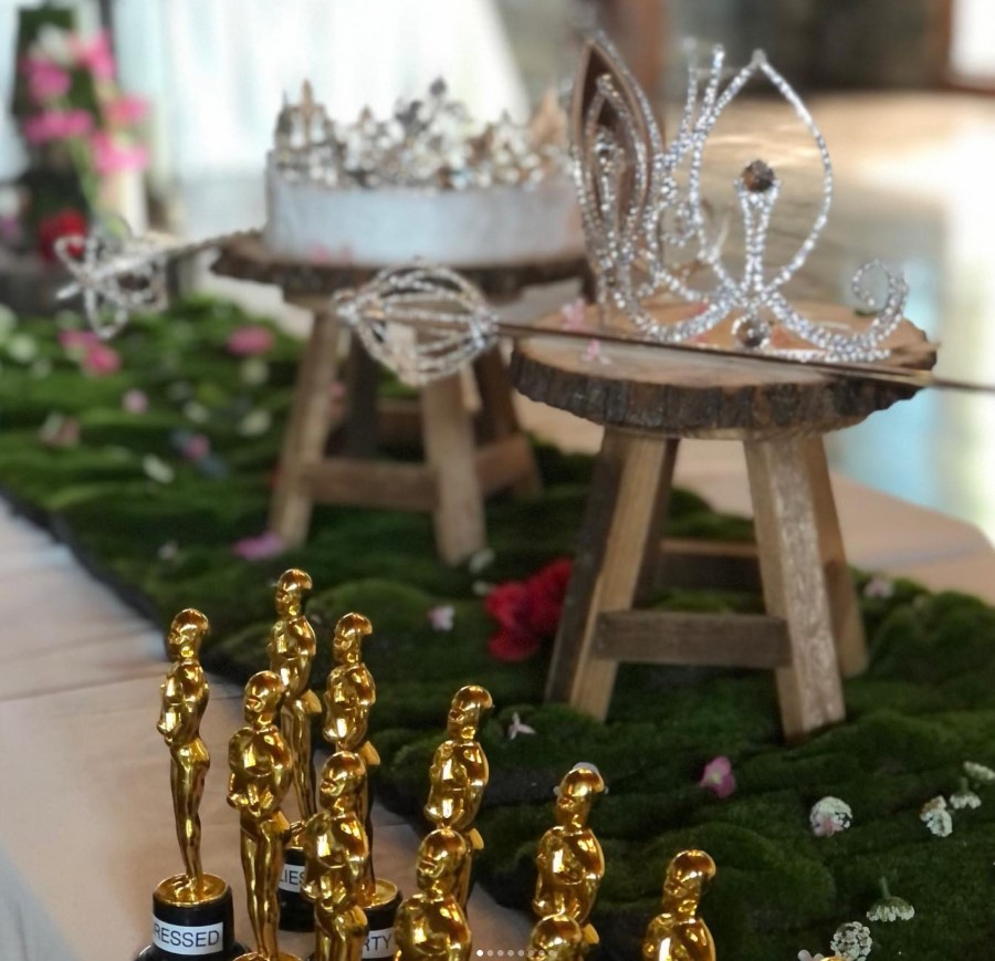 Mini Oscar awards, small flowers, and prom queen crown on table.