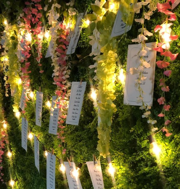 Fake greenery wall with flowers and table numbers for prom event.