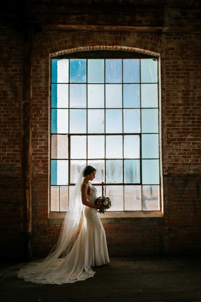 Bride poses for portrait in front of large industrial vintage window.