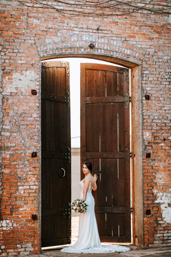 Bride poses for portrait in front of large wooden doors.