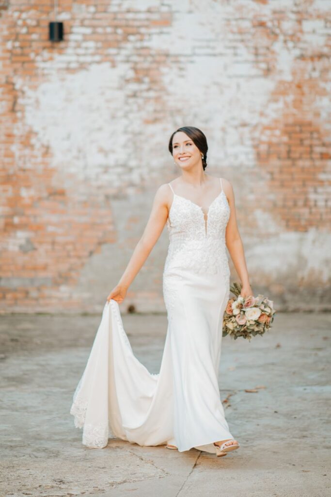 Bride poses for portrait in front of brick wall.