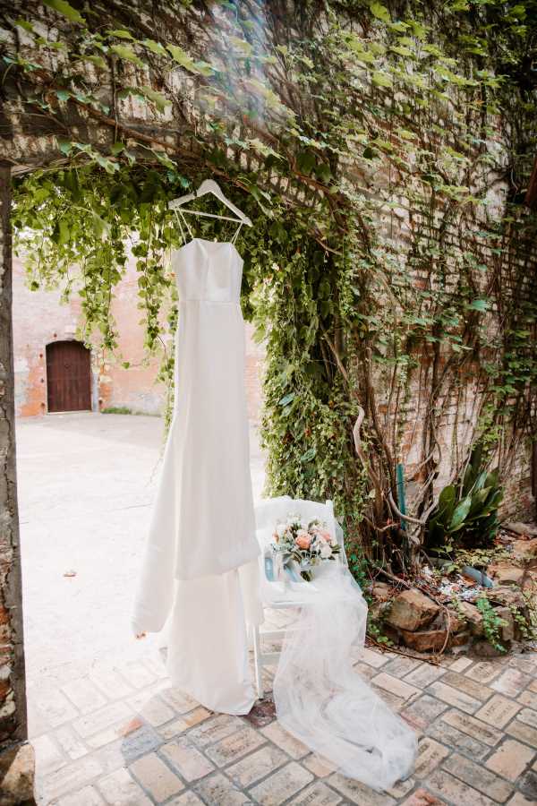Wedding dress and flowers hung on exposed brick with natural greenery in the outdoor Dye Room.
