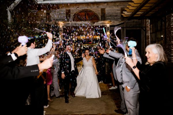 Guests showering bride and groom with bubbles during send-off.