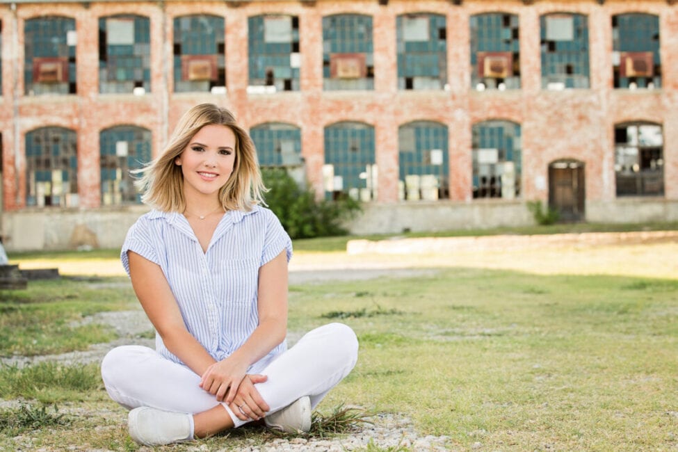 High school girl sitting in a field with The McKinney Cotton Mill building behind her.