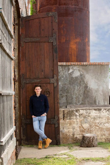 High school guy standing in front of very tall wooden door.