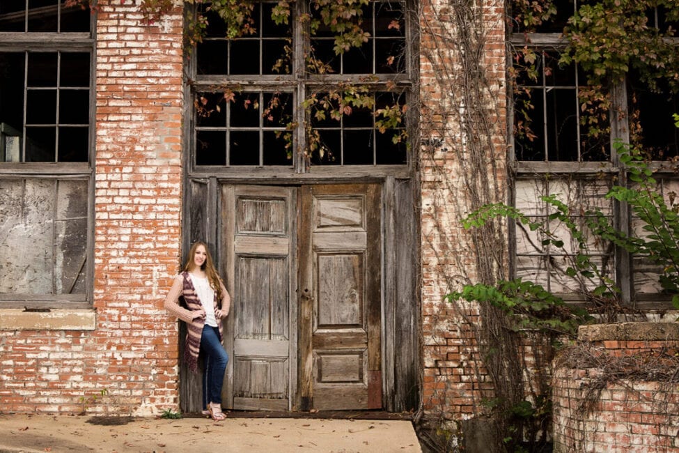 Girl standing in front of exposed brick and natural greenery.