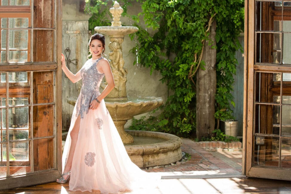 Girl in dress stands in front of fountain and natural greenery outside of the Event Hall.