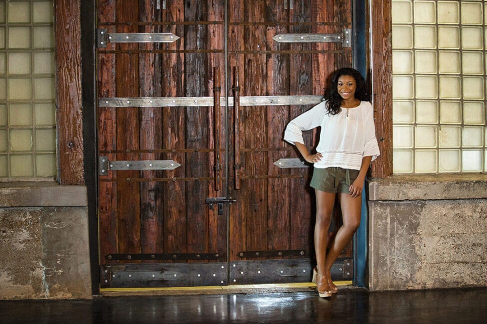 Girl standing in front of two large wooden doors in the Grand Hall of The McKinney Cotton Mill.