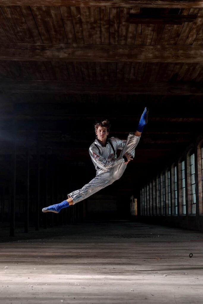 Guy striking a mid-air pose in a large empty industrial warehouse.