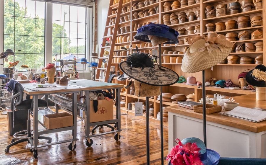 Boutique hat shop with hardwood floors, a work station table, and shelves full of custom hats.