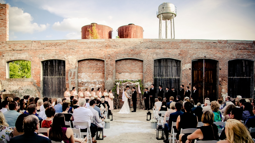 Outdoor wedding ceremony with exposed brick and water tower in background.